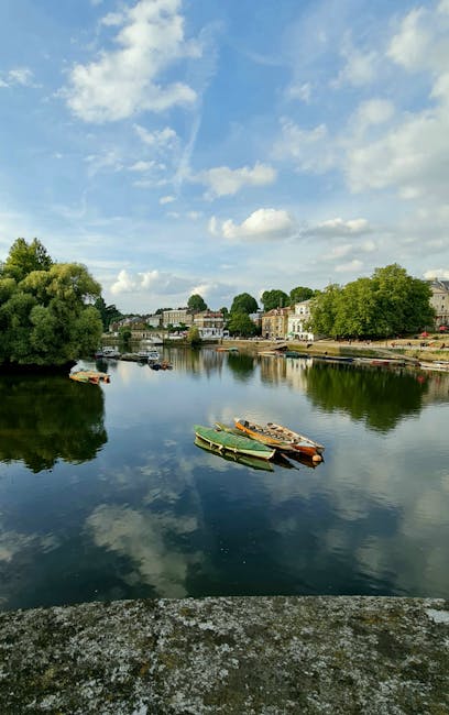Aerial view of Isleworth, showing a blend of residential and commercial buildings along the river Thames. The scene includes a main road with multiple vehicles, such as cars, vans, and a blue delivery